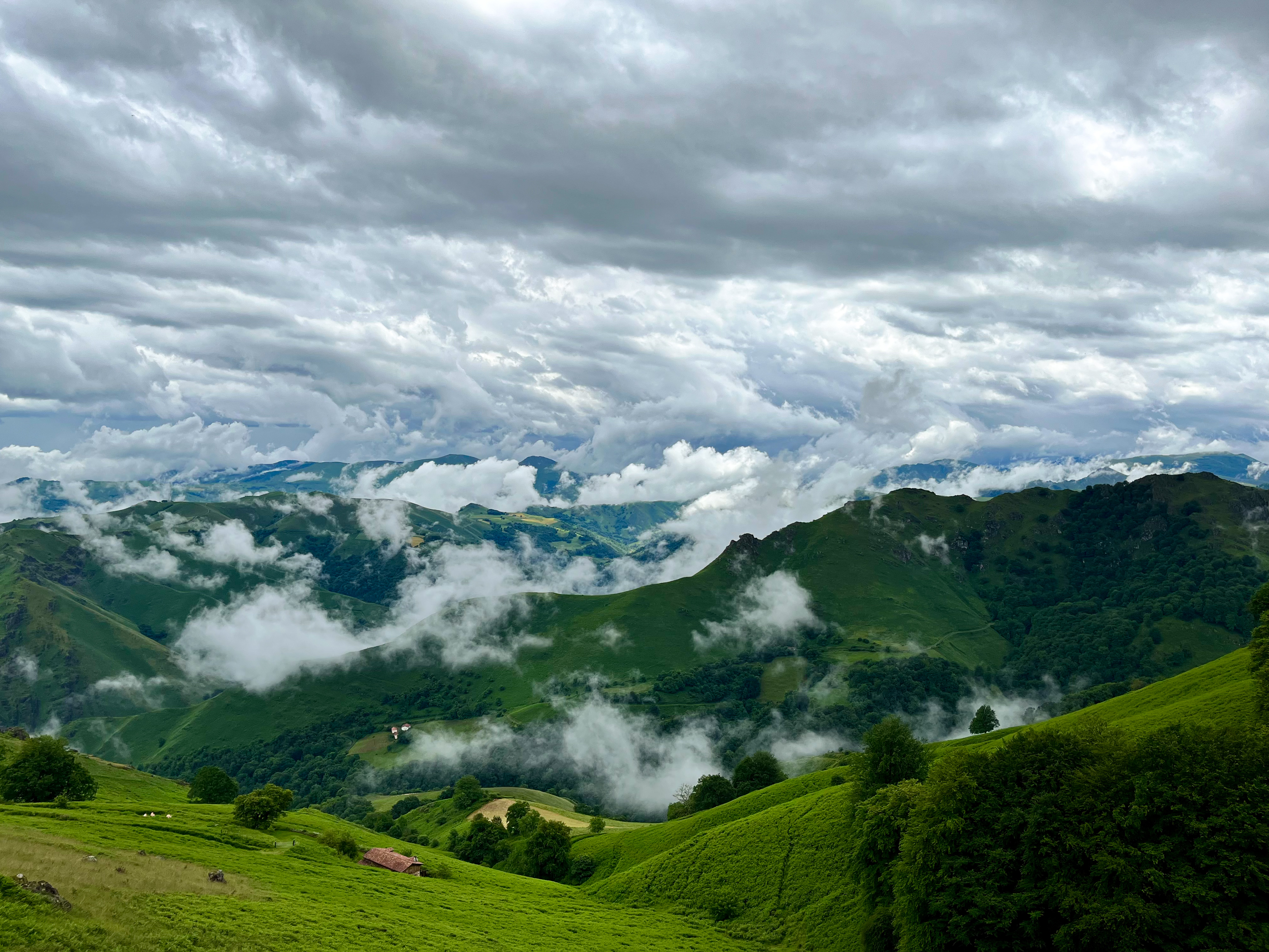 Green Pyrenees ridges with low clouds drifting through the valleys under a vast cloudy sky