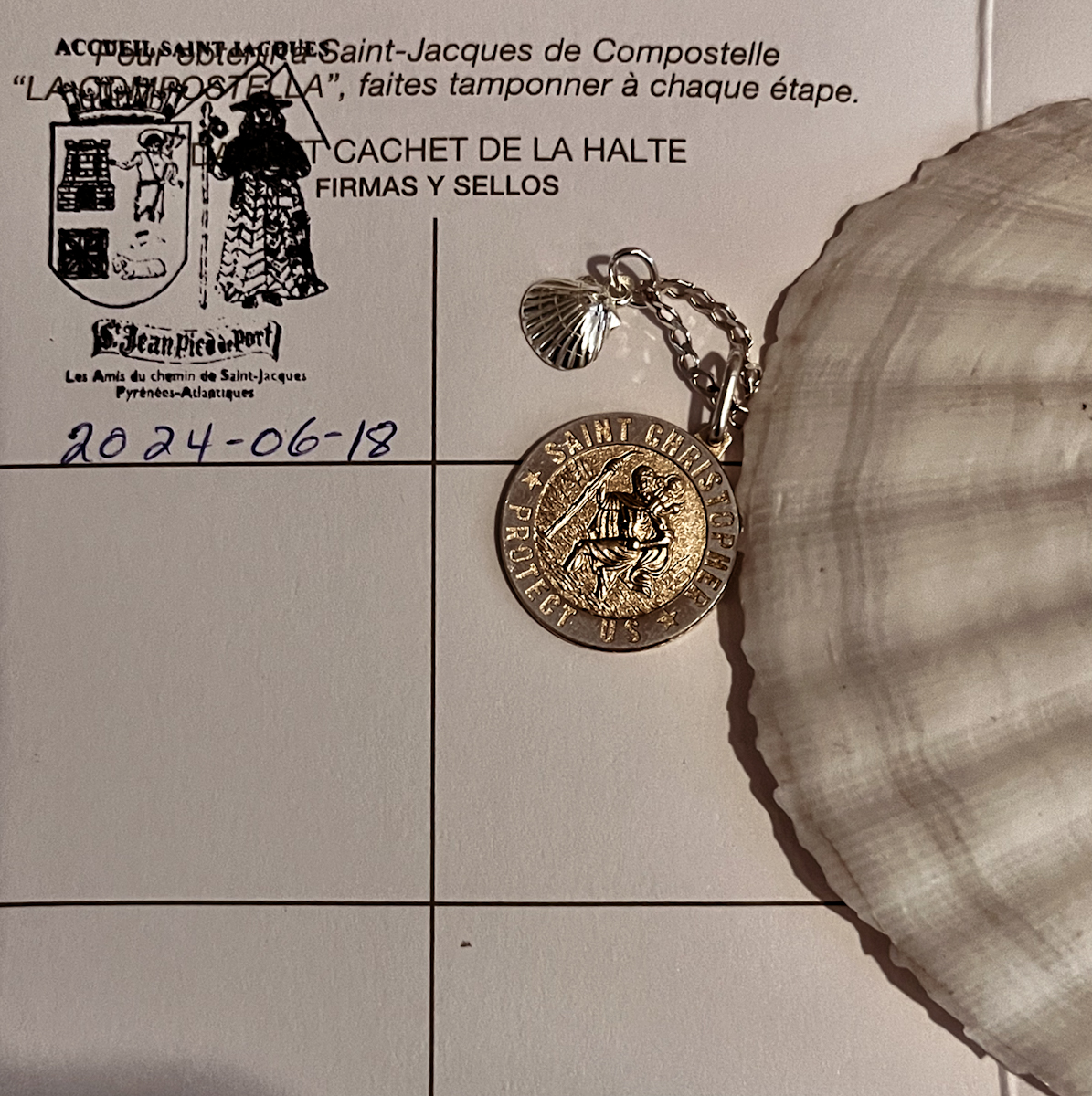 A pilgrim's credential stamped for day one, beside a scallop shell and Saint Christopher medal