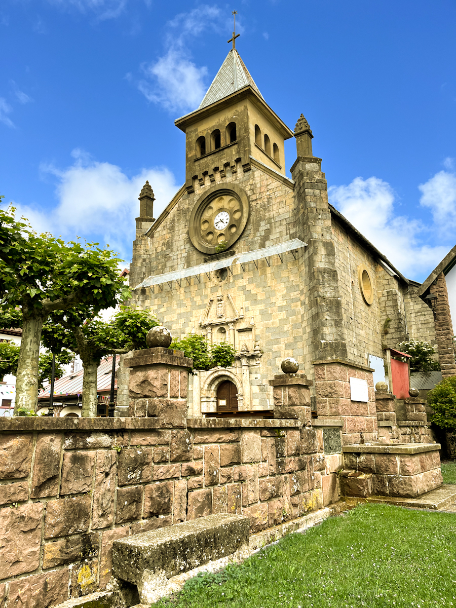 A stone village church with a bell tower under a bright blue sky with white clouds