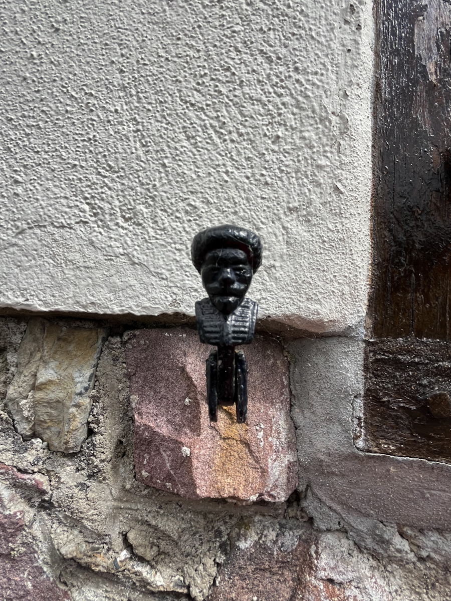 A small antique cast-iron figure of a face mounted at the corner of a stone wall