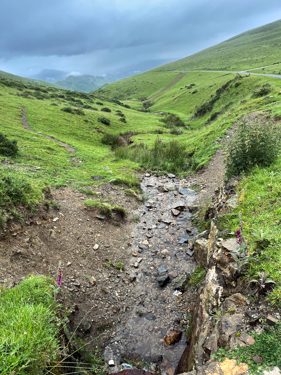 A stream running down a green valley between grassy hills